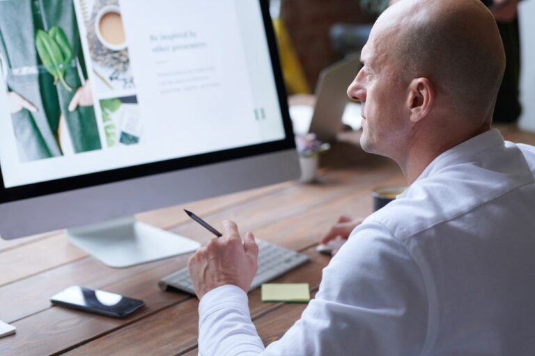 Home 2 Bald man concentrates on work using computer in modern office. Sleek design and digital tools enhance productivity.