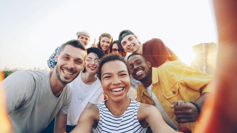 Home 3 A diverse group of friends taking a joyful selfie outdoors during sunset.