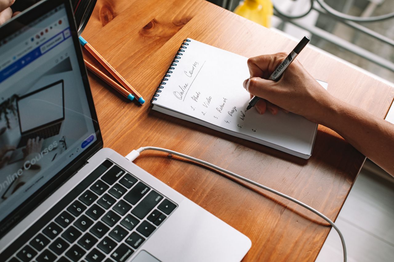 Recursos para diseño estratégico web en empresas 4 A person writing notes while researching online courses on a laptop in a home setting.